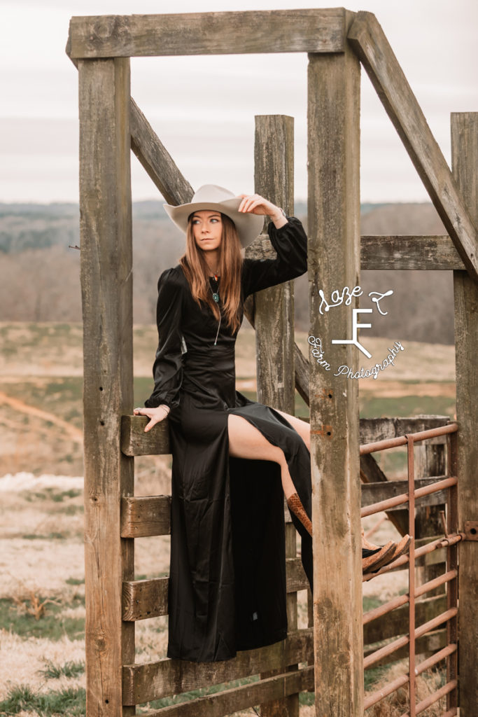 cowgirl in black dress sitting on wooden fence
