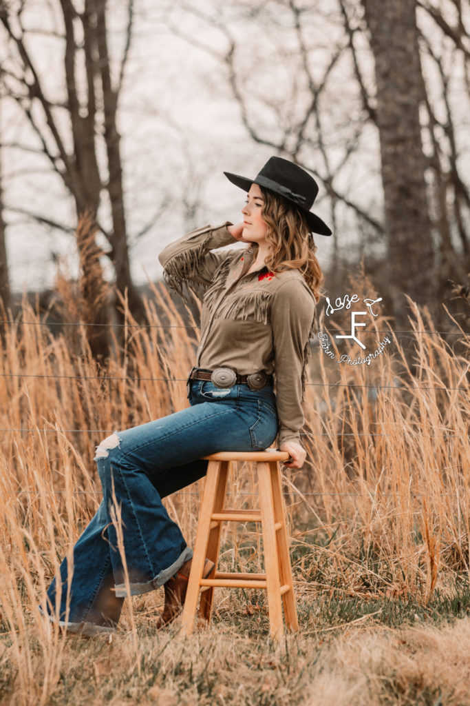 cowgirl sitting on stool in brown grass