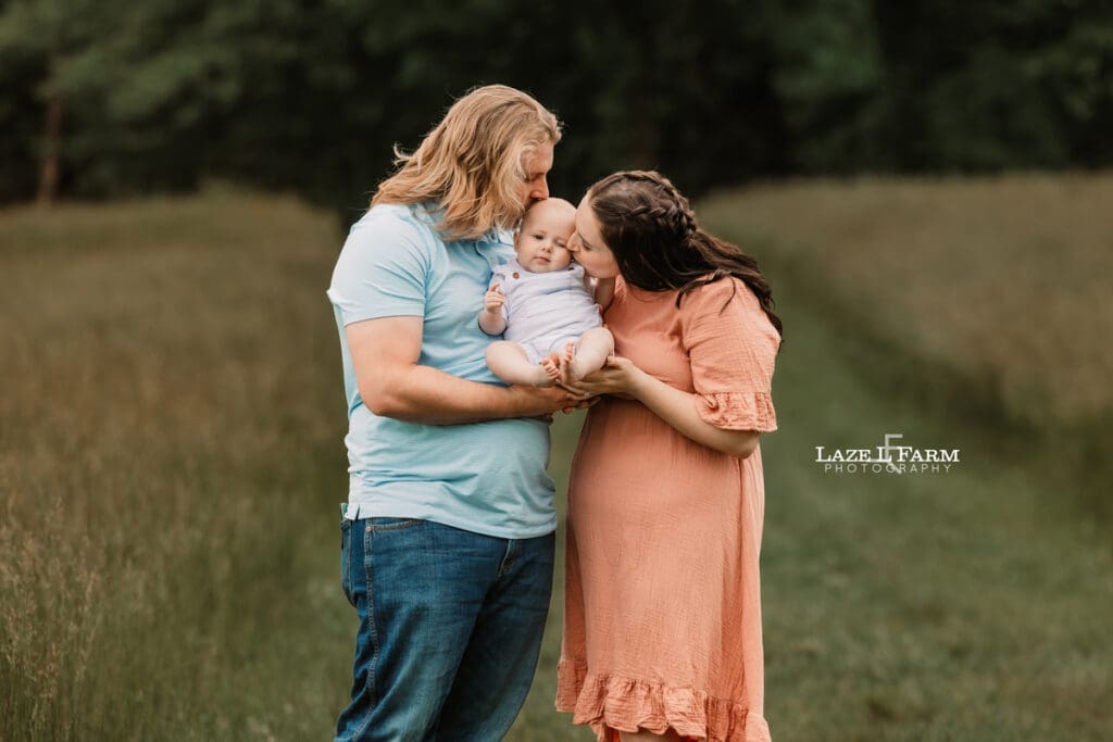 mom and dad kissing son in a field for family pictures