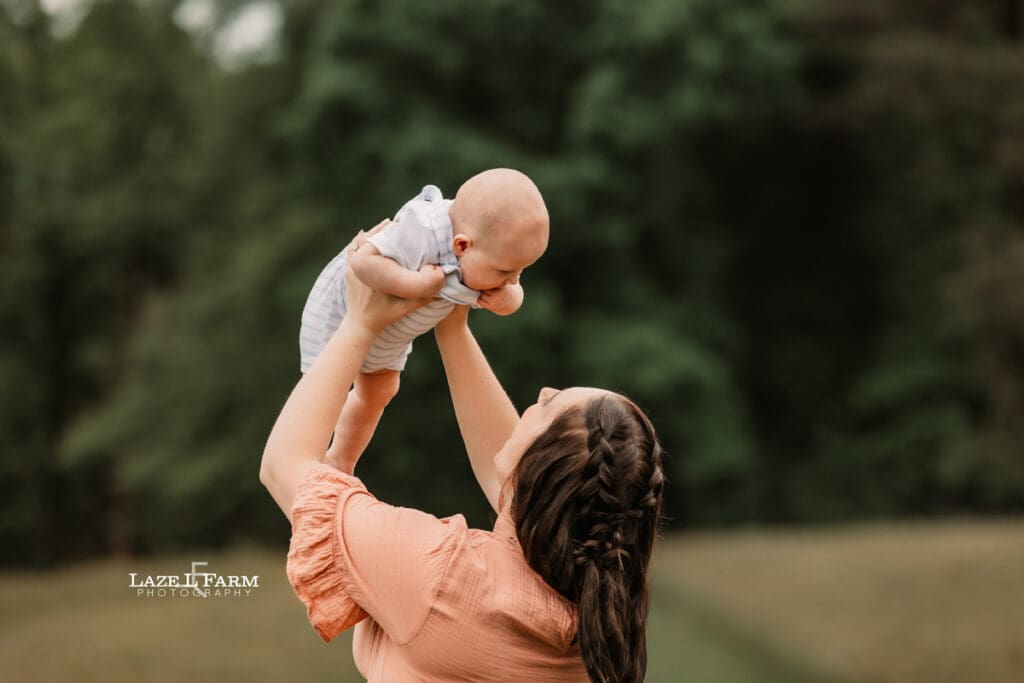 mom holding son up in the air in a field for family pictures