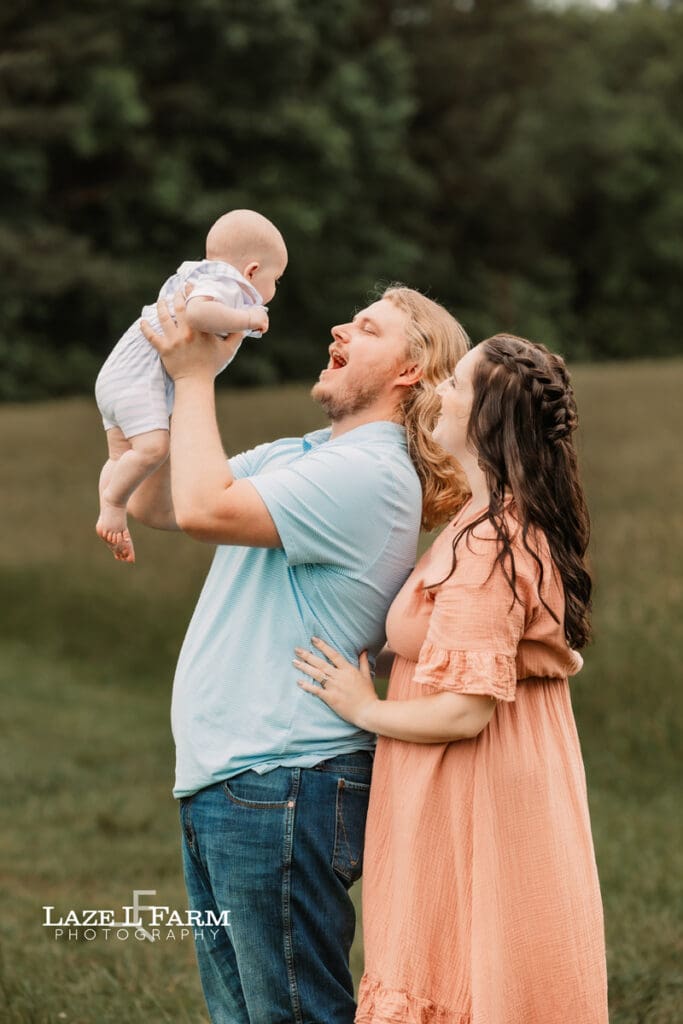 mom and dad holding son in field for family pictures