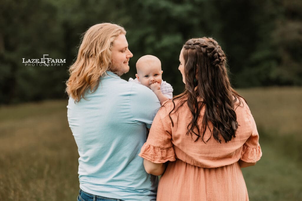 mom and dad holding their son in the field for family pictures