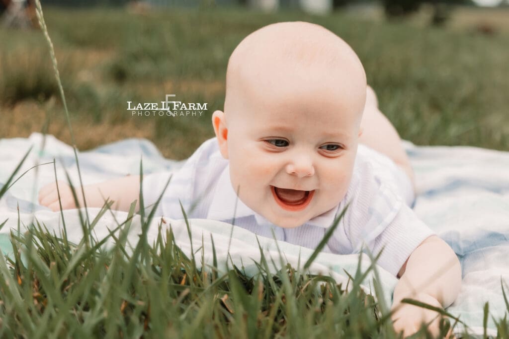 son laying on a blanket in the grass looking at the camera