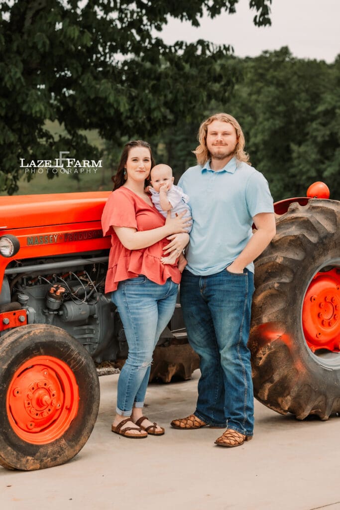 mom, dad, and son standing in front of a tractor for family pictures