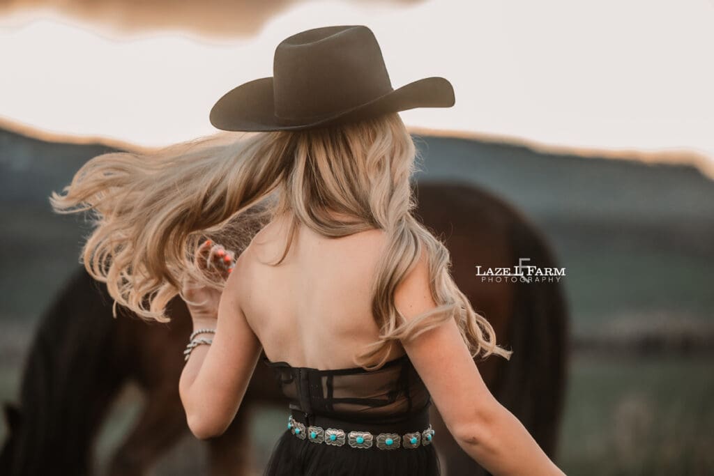 cowgirl in a black dress and black cowboy hat walking away from he camera