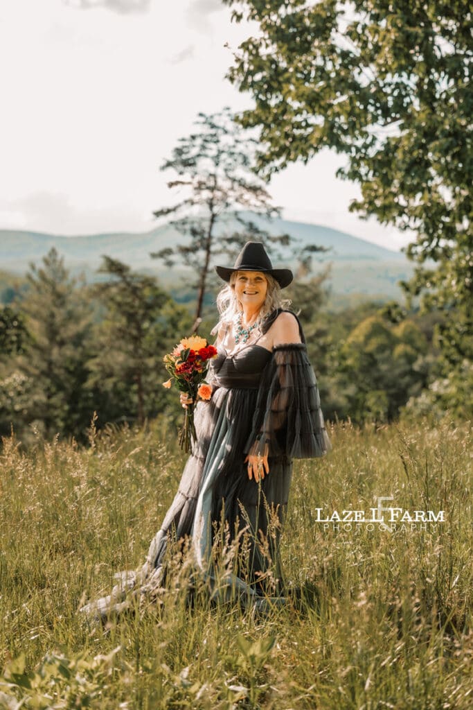 cowgirl standing in a field with flowers at sunset with mountains behind her during a photoshoot