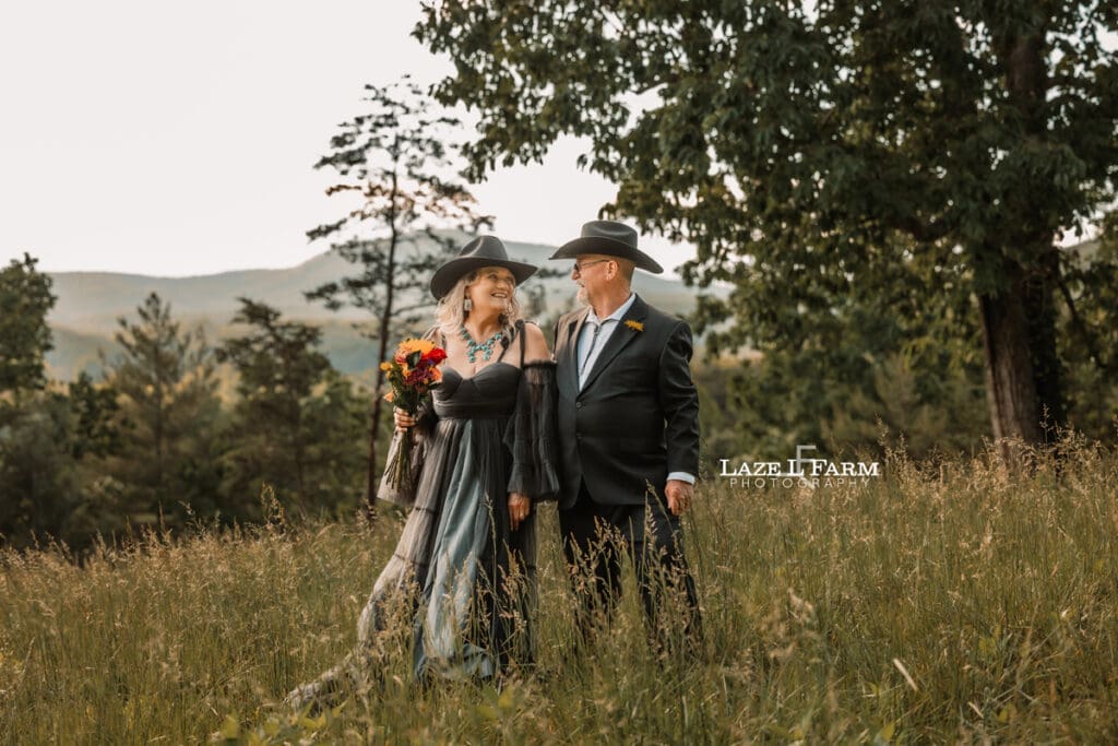 couple standing in a field with flowers with the mountains behind them at sunset