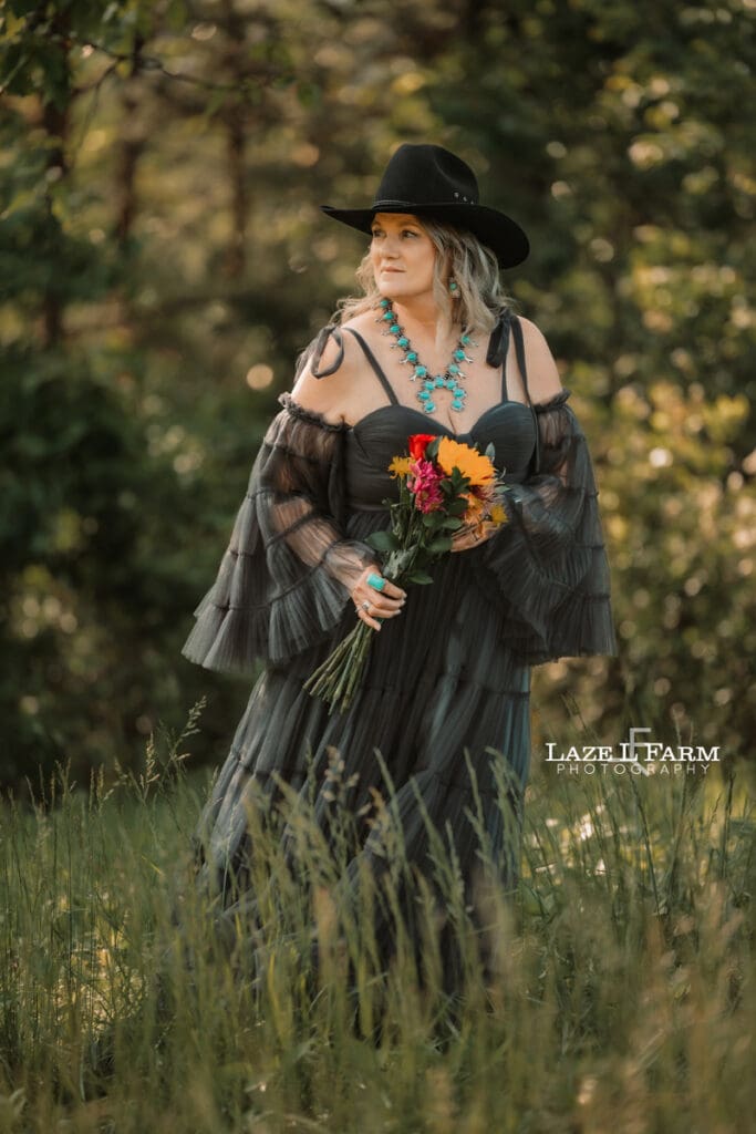 cowgirl standing in a field with flowers at sunset with mountains behind her during a photoshoot