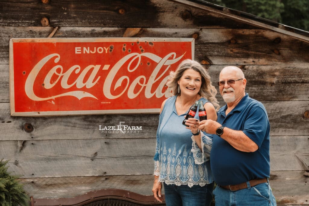 couple standing in front of their barn drinking a coke for family pictures