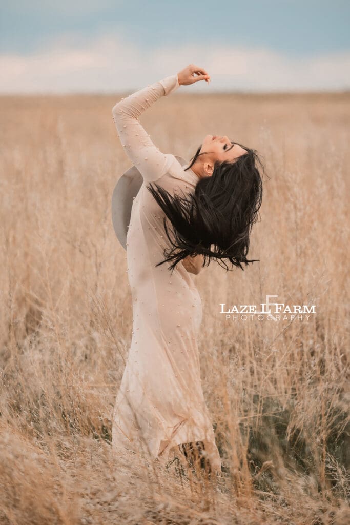 cowgirl standing in a field with a tan dress and tan cowboy hat