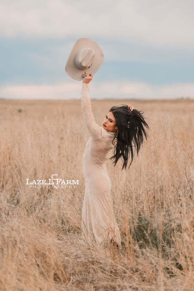 cowgirl standing in a field with a tan dress and tan cowboy hat