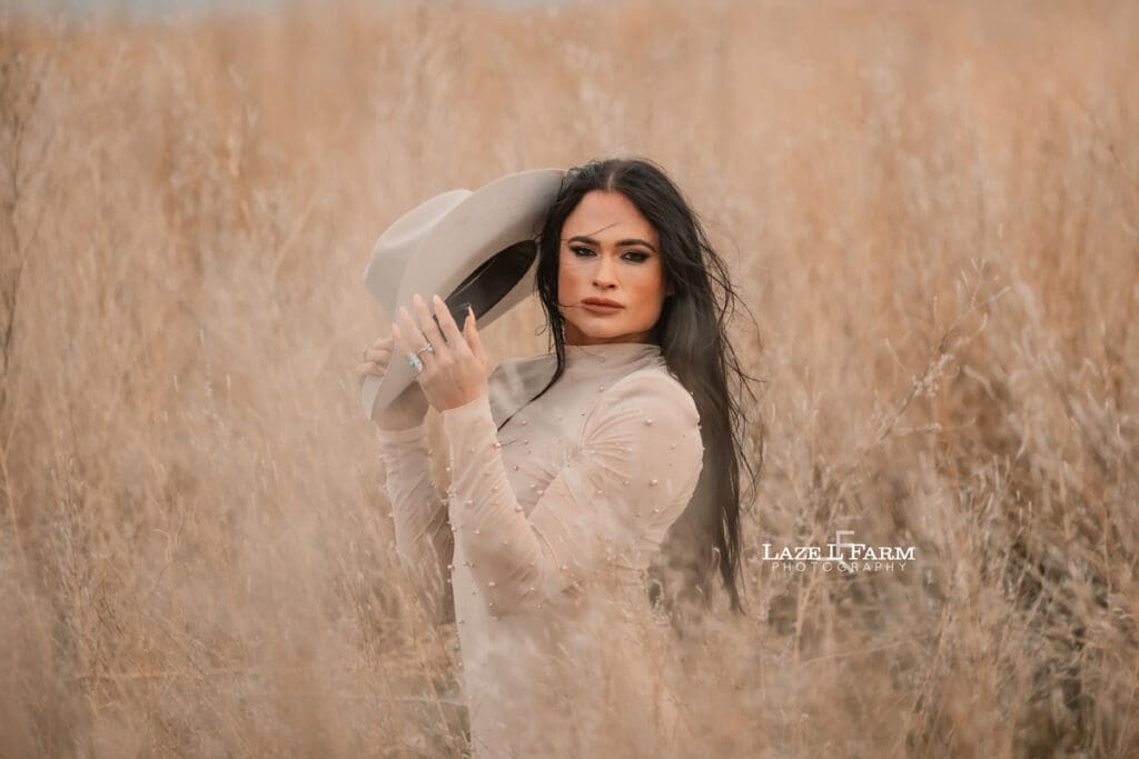 cowgirl standing in a field with a tan dress and tan cowboy hat
