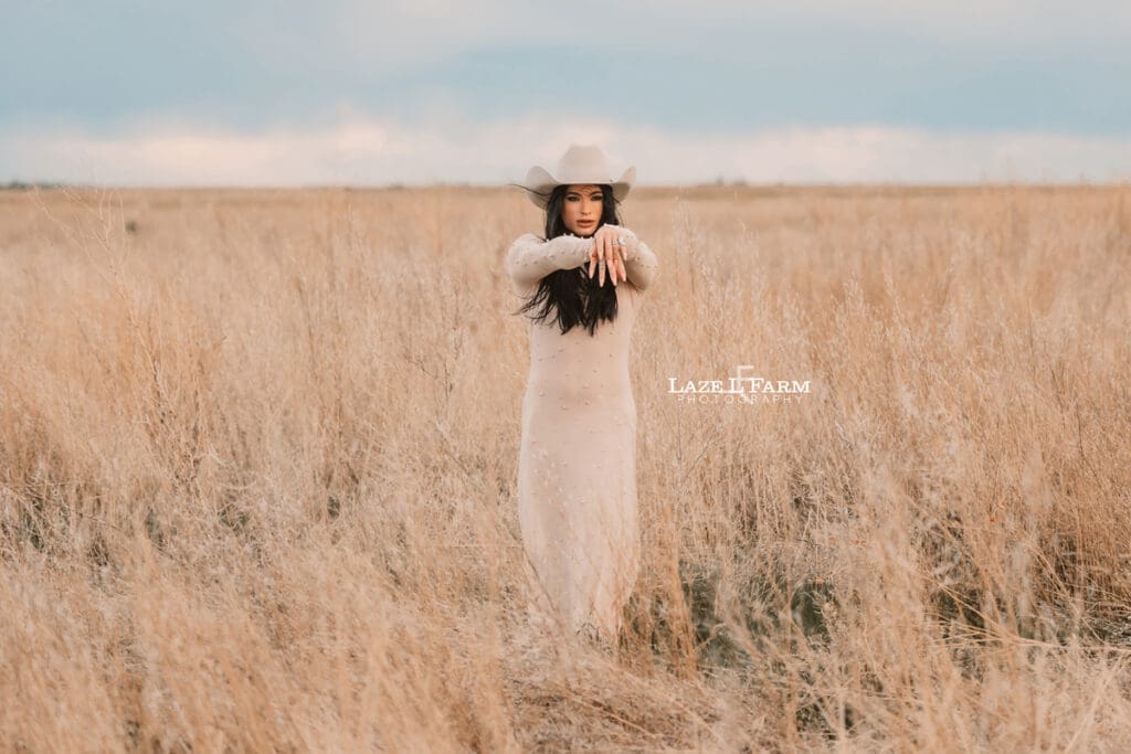 cowgirl standing in a field with a tan dress and tan cowboy hat