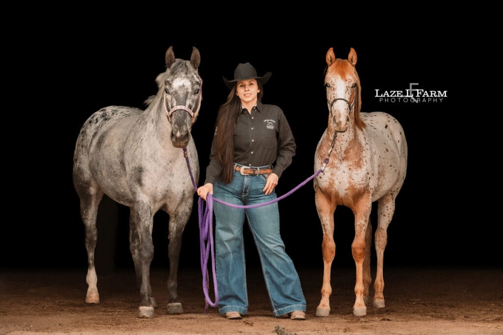 cowgirl with her two appaloosa horses in the barn
