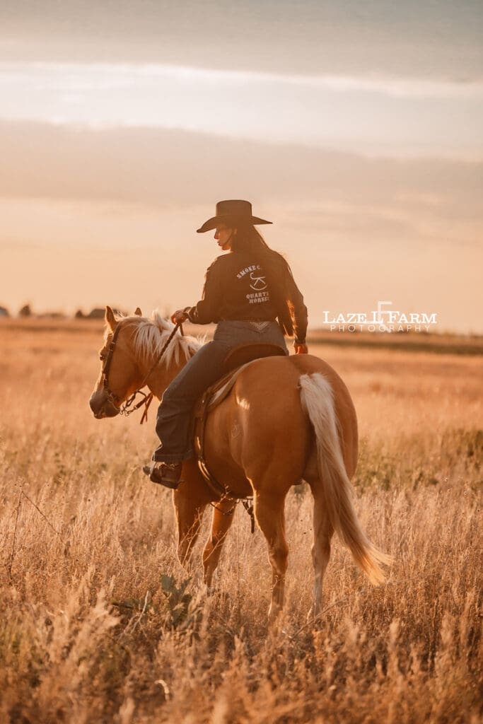 cowgirl riding her palomino horse in an open field at sunset