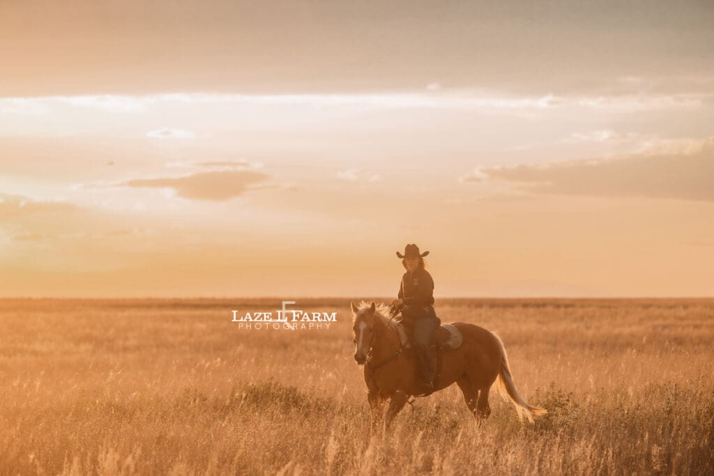 cowgirl riding her palomino horse in an open field at sunset
