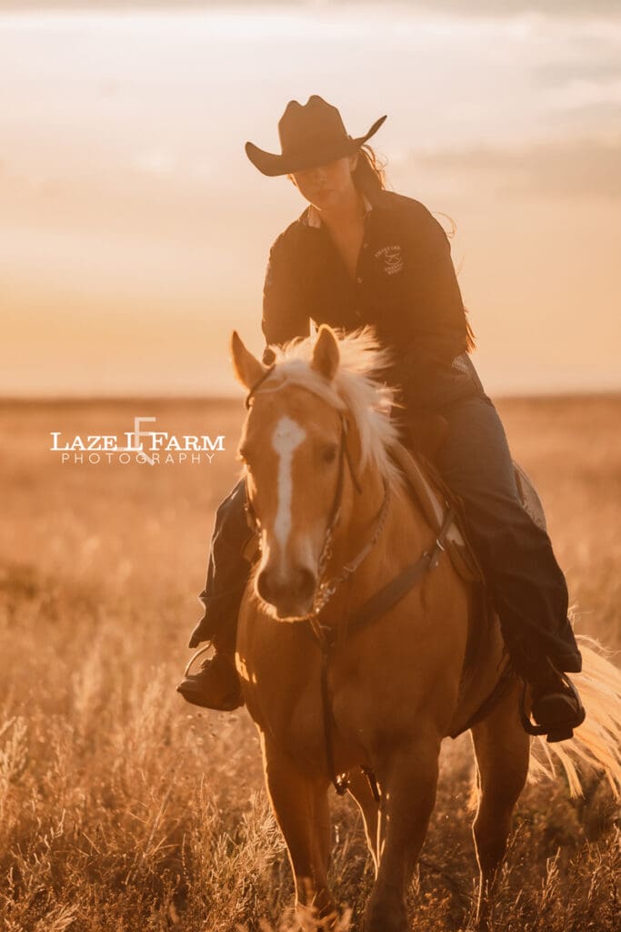 cowgirl riding her palomino horse in an open field at sunset