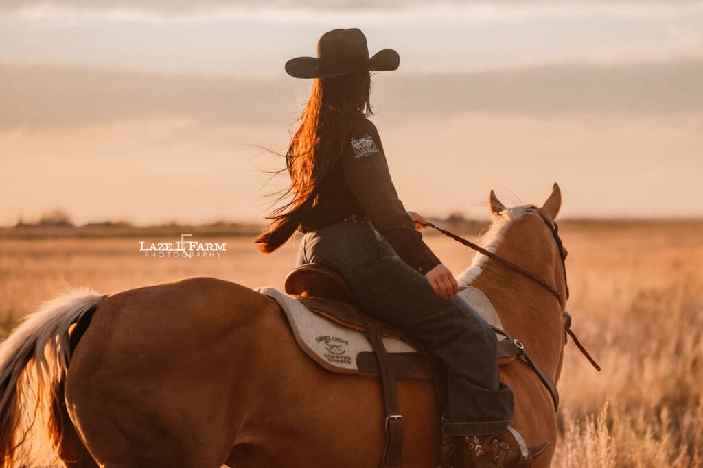 cowgirl riding her palomino horse in an open field at sunset