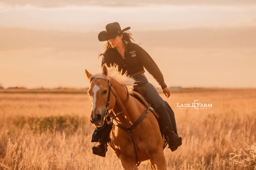 cowgirl riding her palomino horse in an open field at sunset