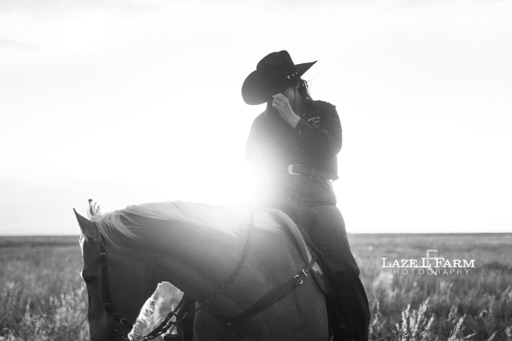 cowgirl riding her palomino horse in an open field at sunset