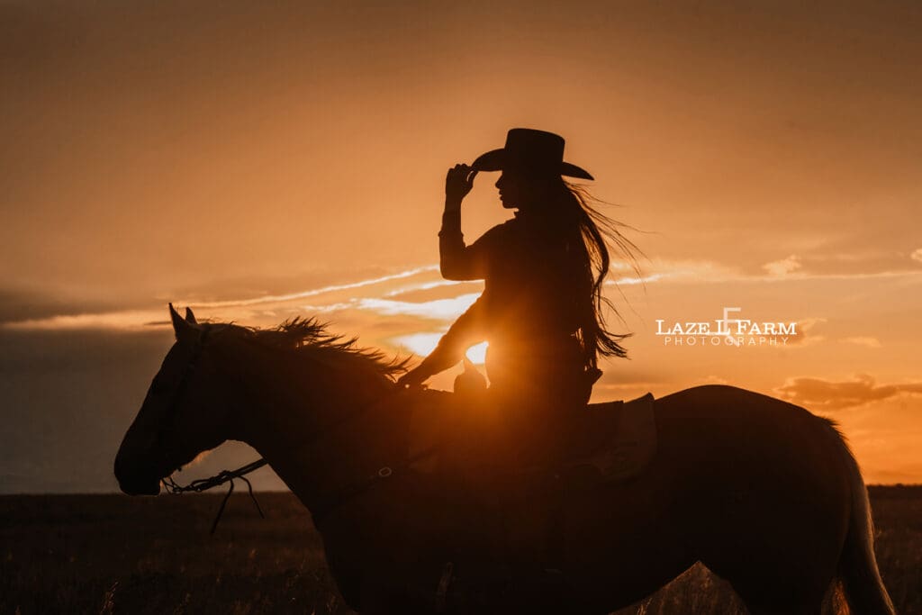 cowgirl riding her palomino horse in an open field at sunset