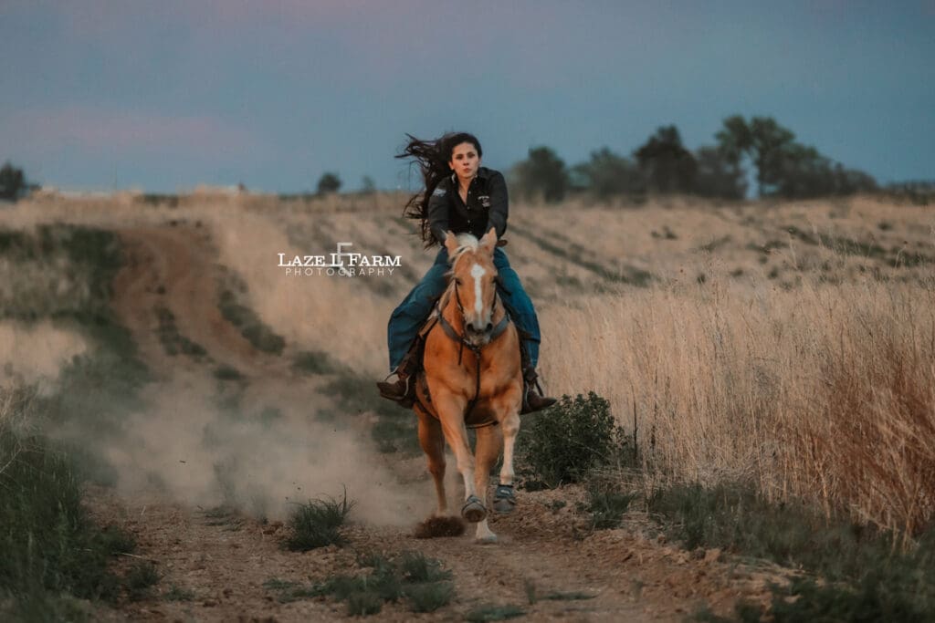 cowgirl riding her palomino horse in an open field at sunset