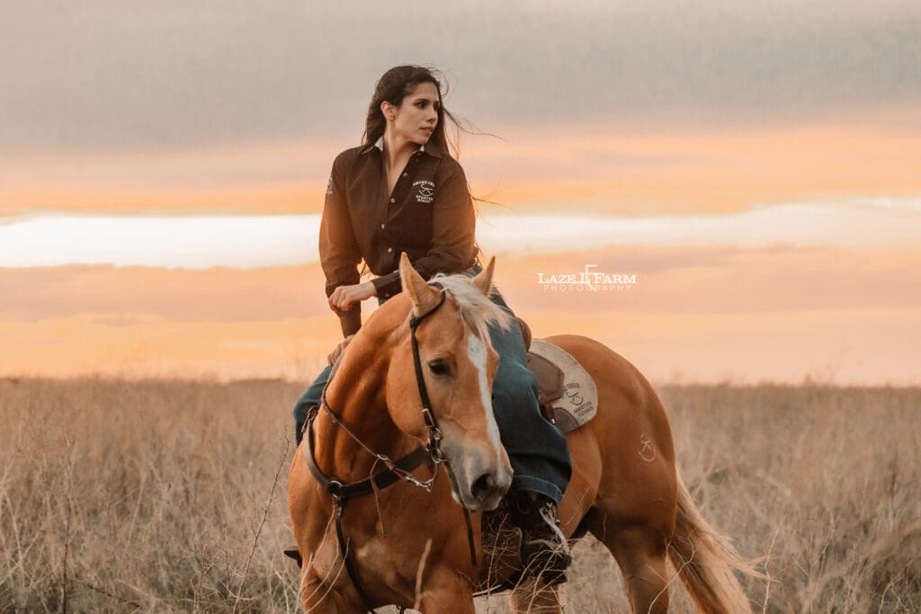 cowgirl riding her palomino horse in an open field at sunset