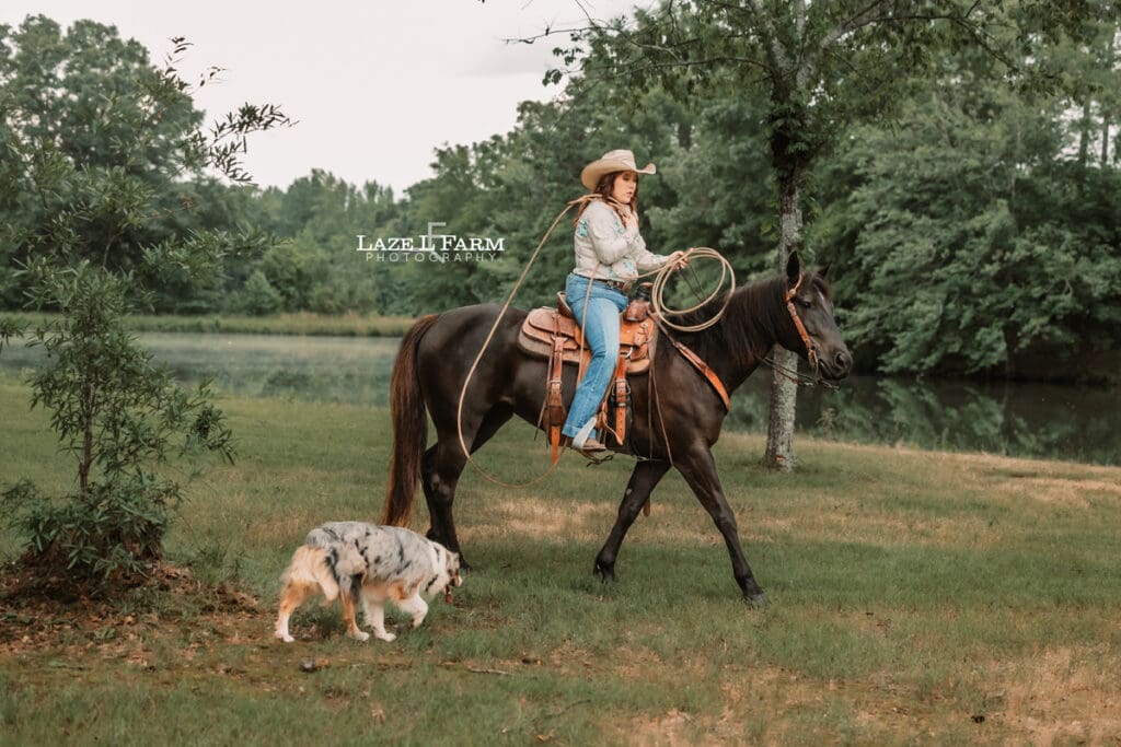 cowgirl riding her horse, swinging a rope with her dog beside of her