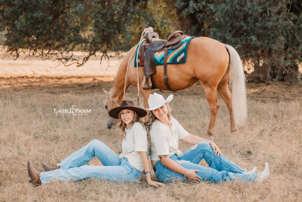 cowgirl best friends sitting back to back in front of the horse