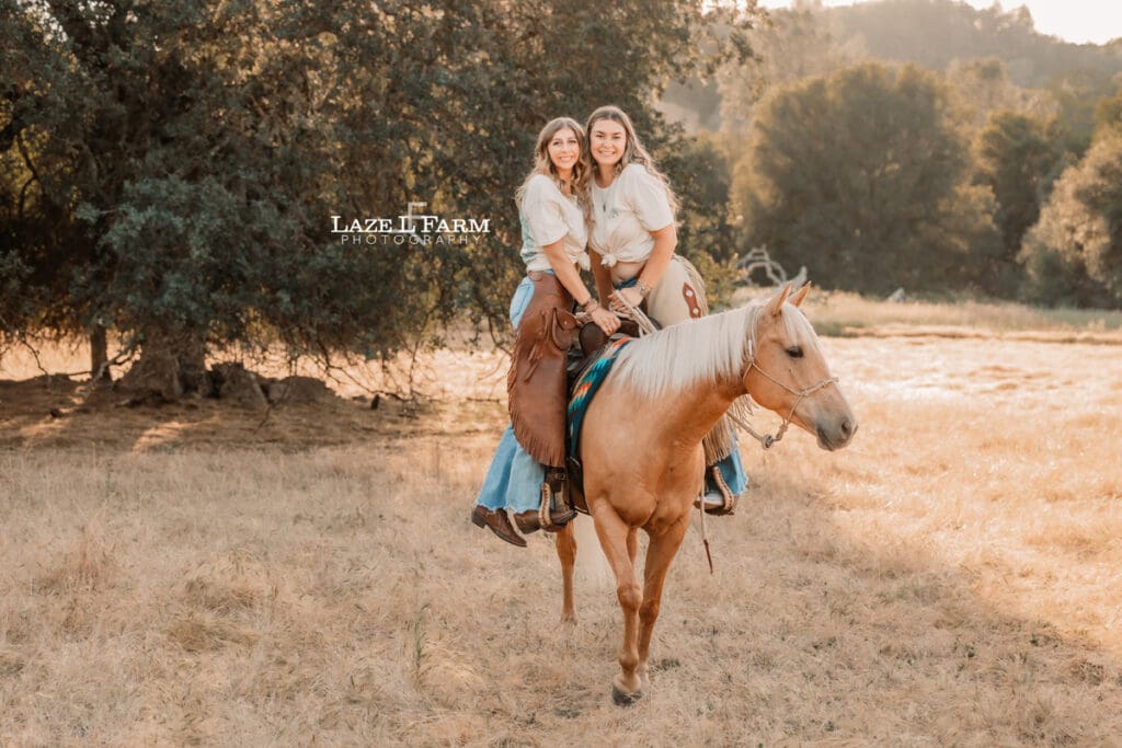 cowgirl best friends standing in different stirrups on the back of a horse