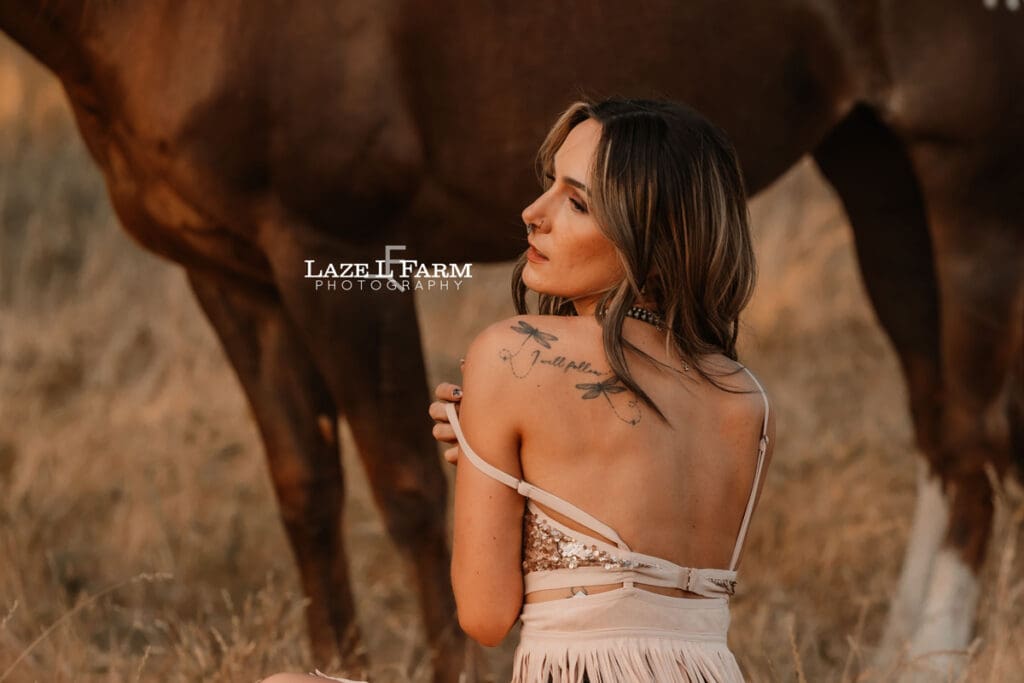cowgirl with a sparkly dress and boots in a field with a horse