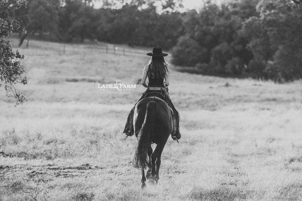 cowgirl riding her horse through a field at sunset