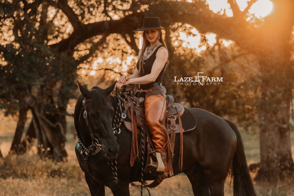cowgirl riding her horse through a field at sunset