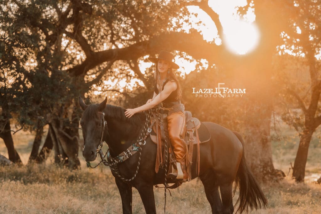 cowgirl riding her horse through a field at sunset