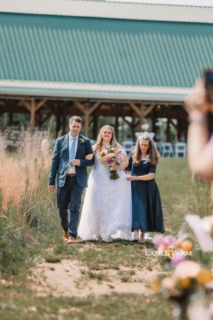 Bride walking down the aisle with her mom and brother during her wedding at Woodside Farm in Graham, NC with pictures by Laze L Farm Photography