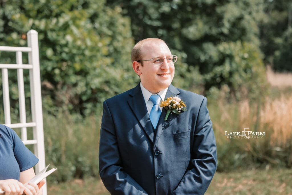 Groom waiting on the bride to walk down the aisle during their wedding at Woodside Farm in Graham, NC with pictures by Laze L Farm Photography