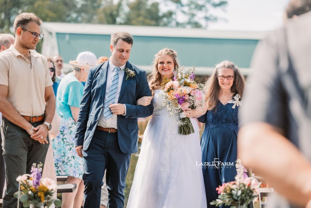 Bride walking down the aisle with her mom and brother during her wedding at Woodside Farm in Graham, NC with pictures by Laze L Farm Photography