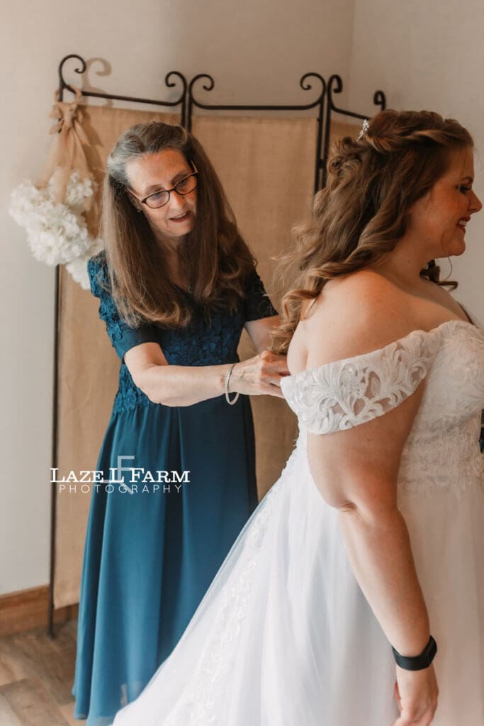Mother of the bride helping her with her dress during her wedding at Woodside Farm in Graham, NC with pictures by Laze L Farm Photography