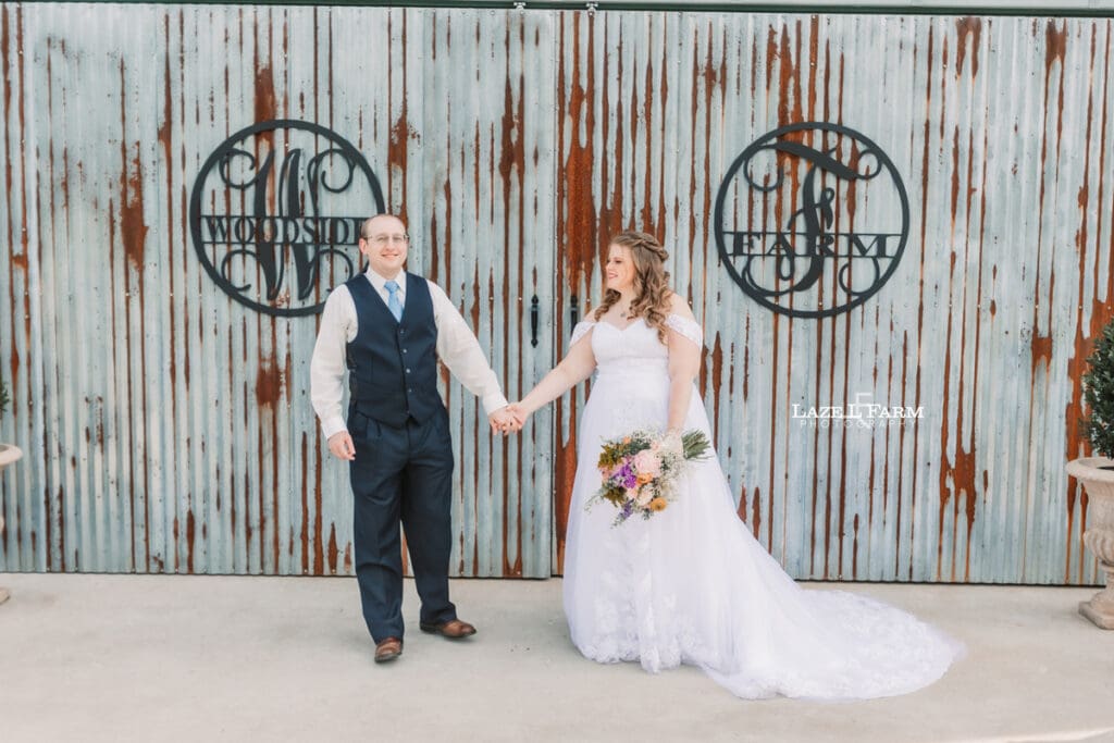 Bride and Groom holding hands in front of their venue at Woodside Farm in Graham, NC with pictures by Laze L Farm Photography