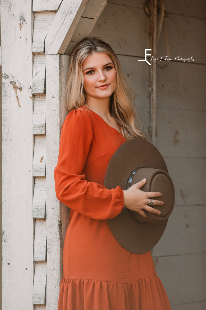 Laze L Farm Photography | Senior Photography | Equine Photography | standing against a building holding her hat