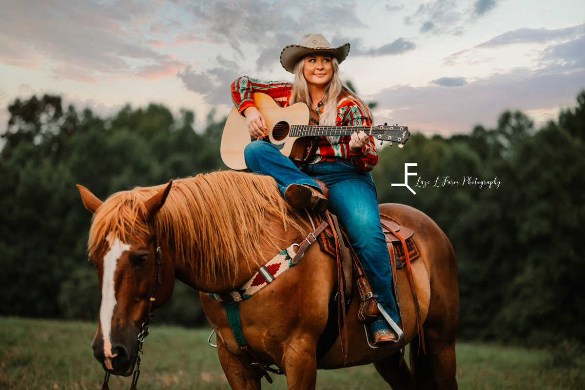 girl sitting on horse with hat playing guitar 