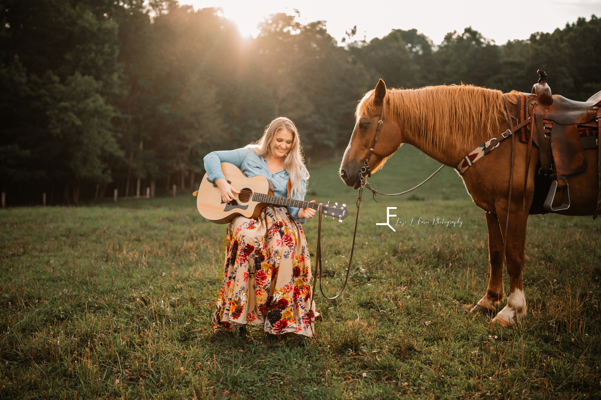 girl playing guitar with a horse in a field