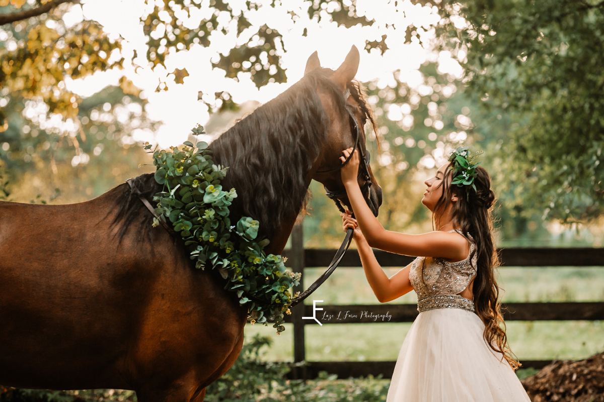 girl in white dress with greenery crown petting horse 