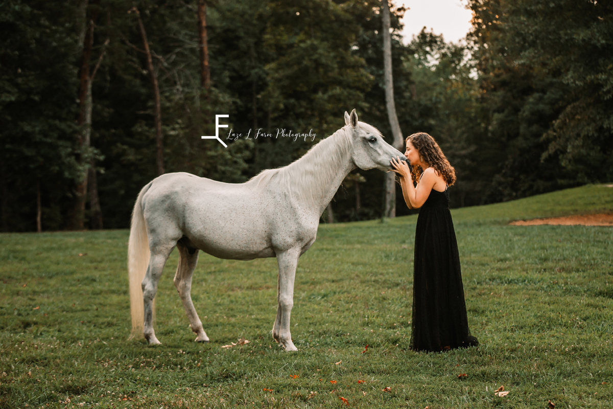 girl in black dress kissing gray horse in field