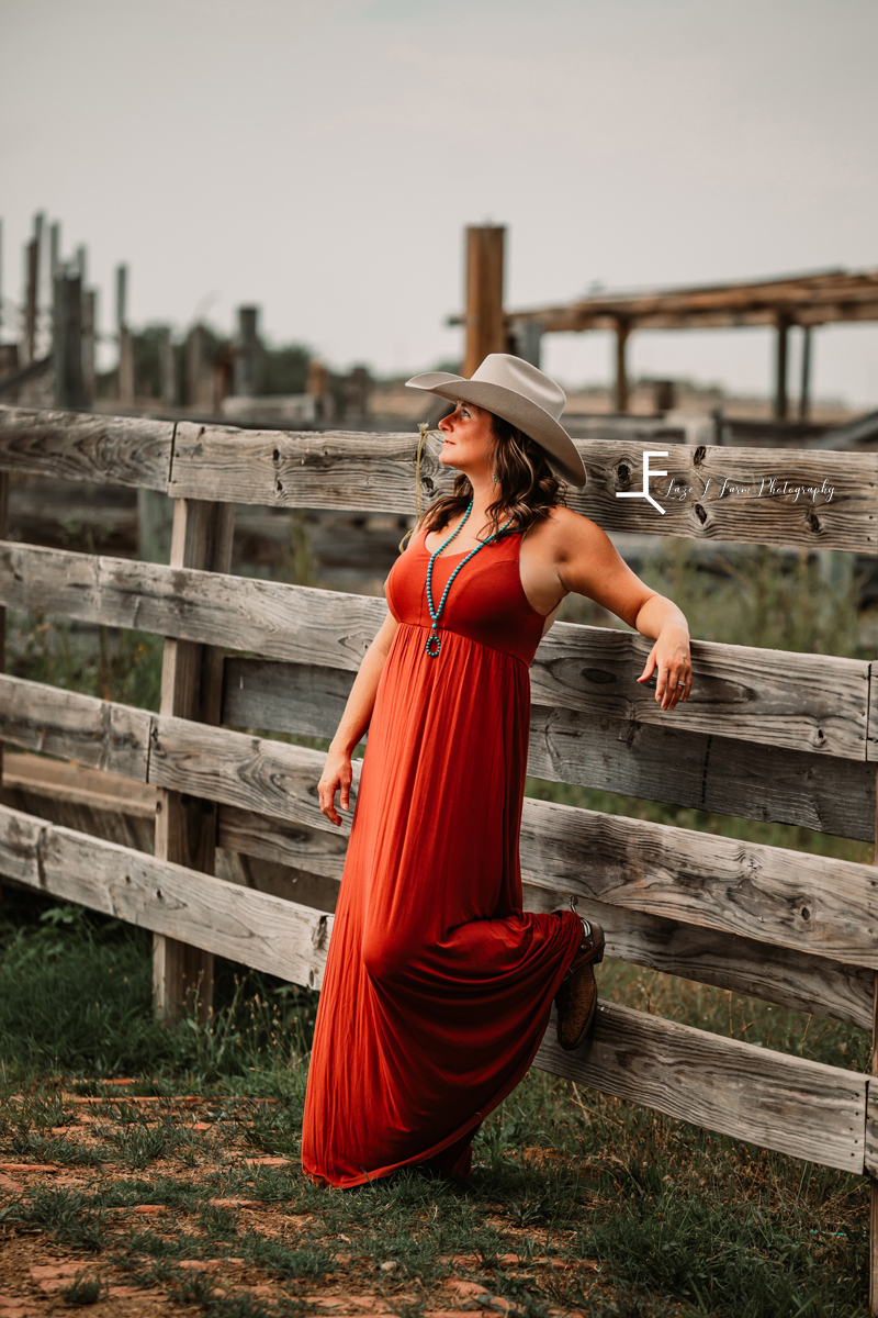 cowgirl in red dress leaning on stockyard fence