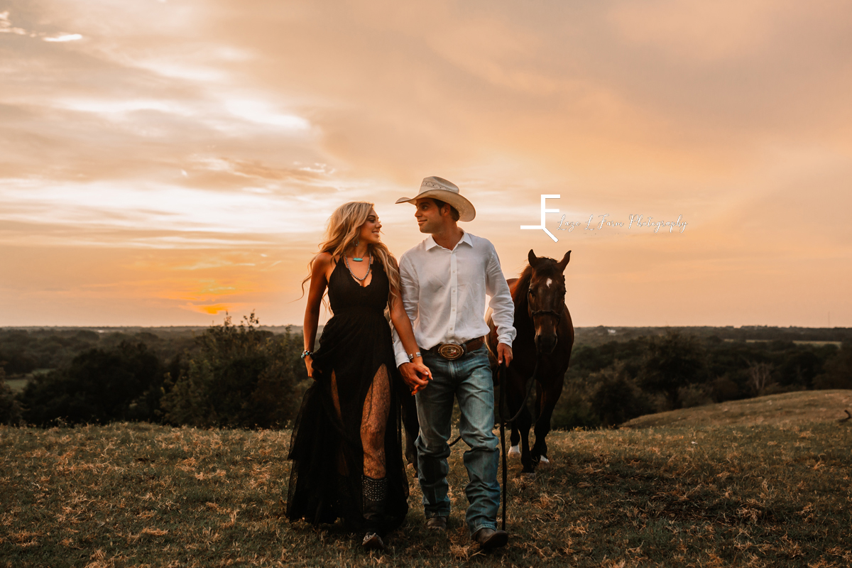cowboy and wife wearing black dress walking with horse