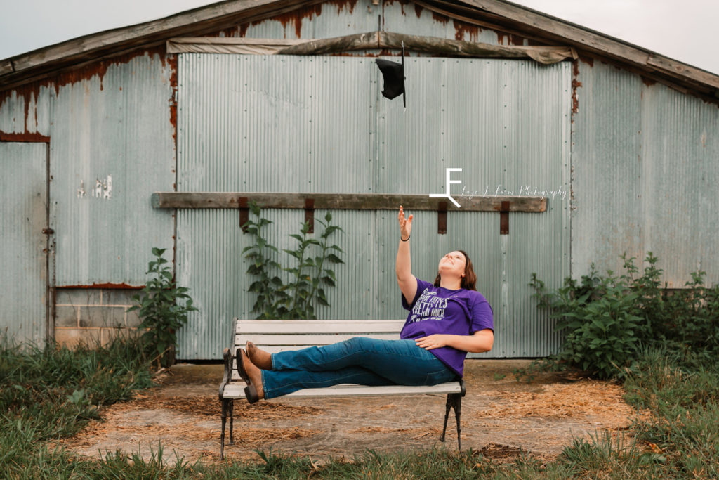 girl throwing graduation cap leaning back on bench