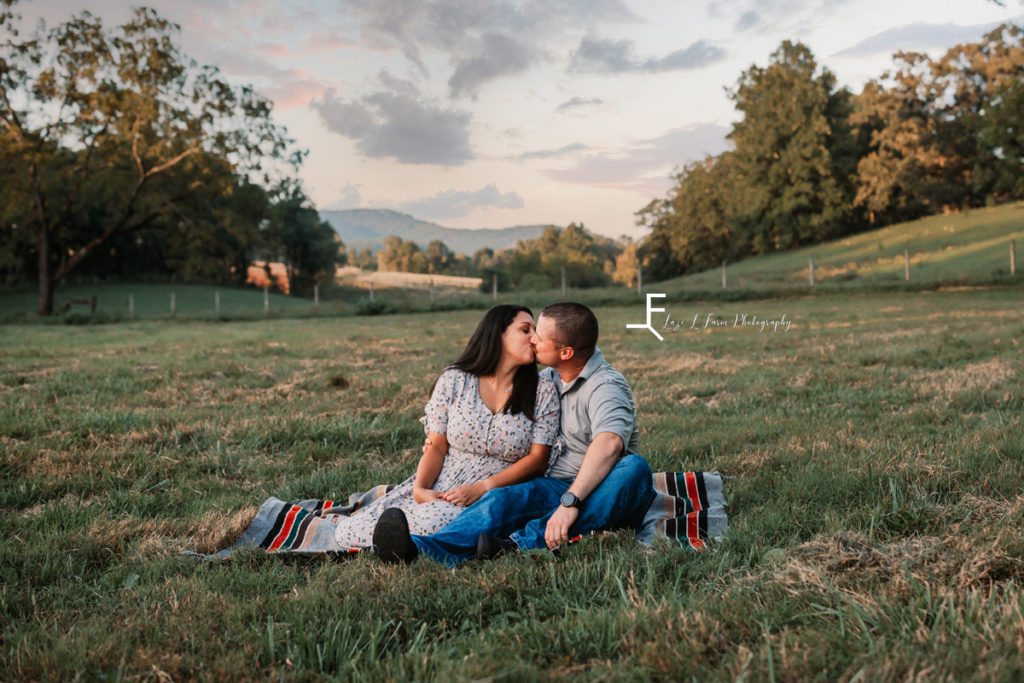 husband and wife sitting in a field kissing