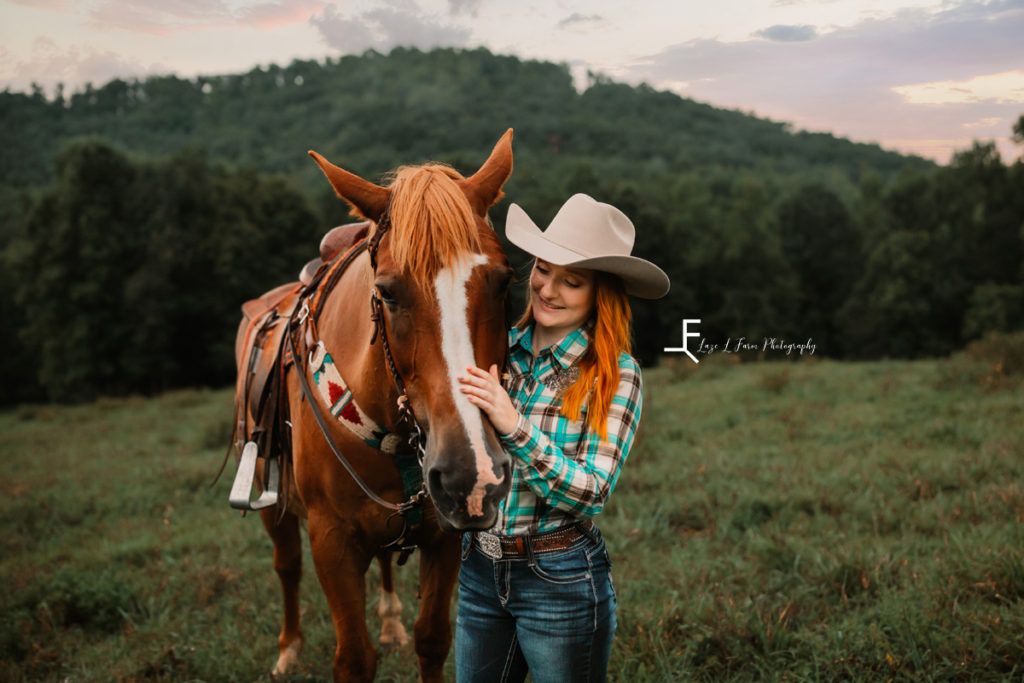 redhair cowgirl petting horse with mountain in back