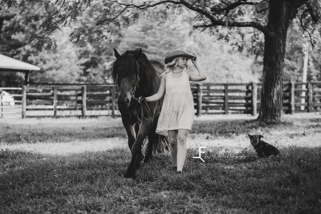 cowgirl looking away with dog and horse in black and white